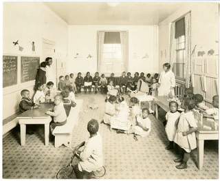 Image via Wikimedia Commons (note the white dolls the girls are playing with)